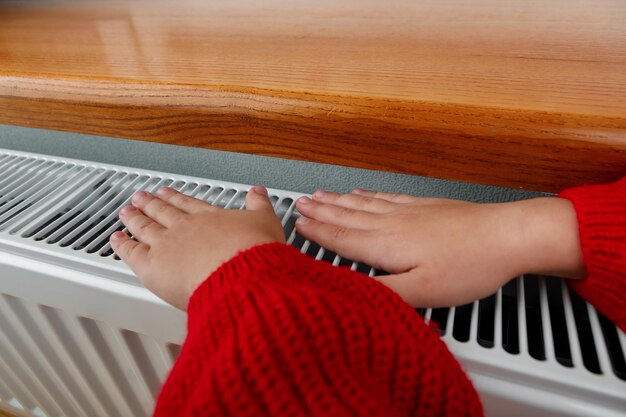 Una bambina si scalda mani e piedi su un termosifone