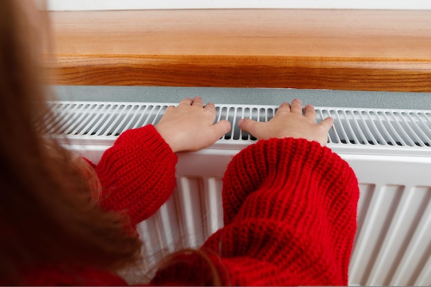 Una bambina si scalda mani e piedi su un termosifone