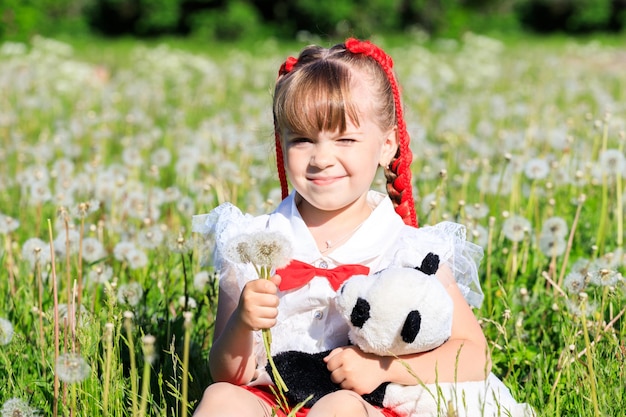 Una bambina si siede nella natura in estate con un panda giocattolo. Foto di alta qualità