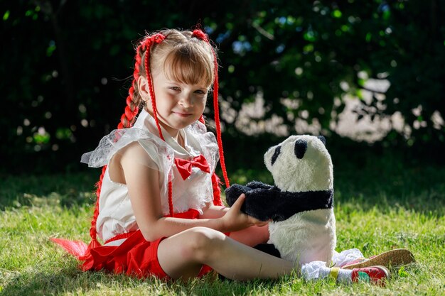 Una bambina si siede nella natura in estate con un panda giocattolo. Foto di alta qualità