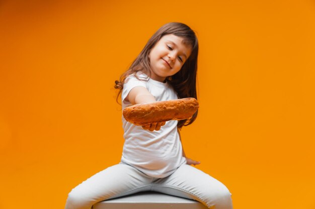 Una bambina si siede su un cubo su uno sfondo giallo e mangia una pagnotta cibo sano prodotti naturali pane