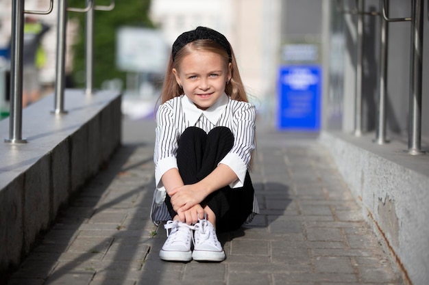 Una bambina si siede sul marciapiede in strada Un bambino in città