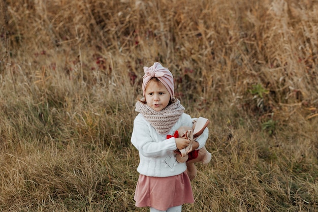 Una bambina si trova in una radura. Autunno dorato. il bambino è in piedi sull'erba con un maglione bianco lavorato a maglia e tiene in mano un peluche