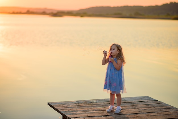 Una bambina soffia bolle sul molo vicino al lago