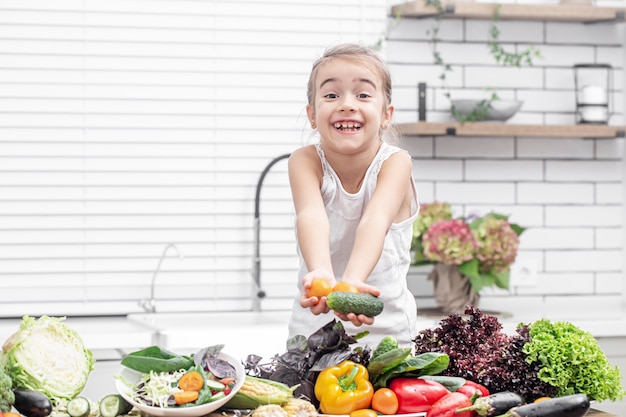 Una bambina sorride e tiene in mano la verdura fresca mentre prepara un'insalata.