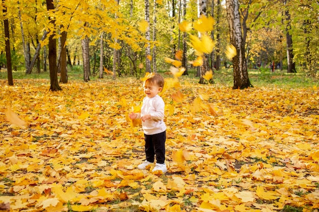 Una bambina sorridente con gli occhi chiusi sta nel parco autunnale Le foglie d'acero gialle le cadono addosso