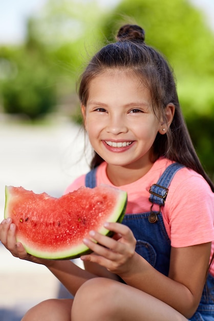 Una bambina sorridente e carina mangia un'anguria in una soleggiata giornata estiva