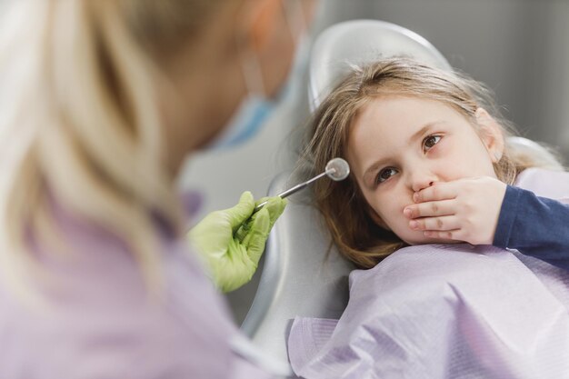 Una bambina spaventata su una sedia del dentista e tiene la bocca chiusa per impedire al dentista di lavorare.