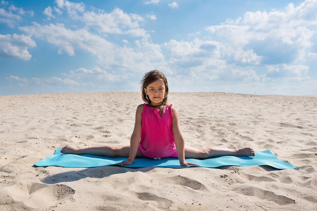 Una bambina sta facendo ginnastica sulla spiaggia il bambino si siede su uno spago