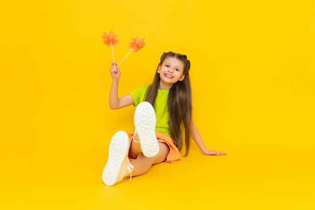 Una bambina sta giocando con fiori di carta su bastoncini Un mulino di origami Il bambino felice tiene i mestieri di carta La creatività dei bambini Un bel bambino è seduto su uno sfondo giallo isolato