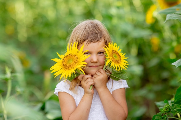 Una bambina sta giocando con i fiori di girasole in un campo con i girasoli