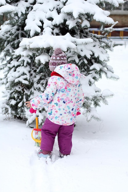 Una bambina sta giocando nella neve vicino all'albero di Natale nel cortile