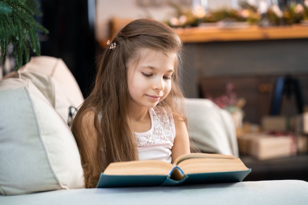 Una bambina sta leggendo un libro interessante. Istruzione e tempo libero dei bambini.