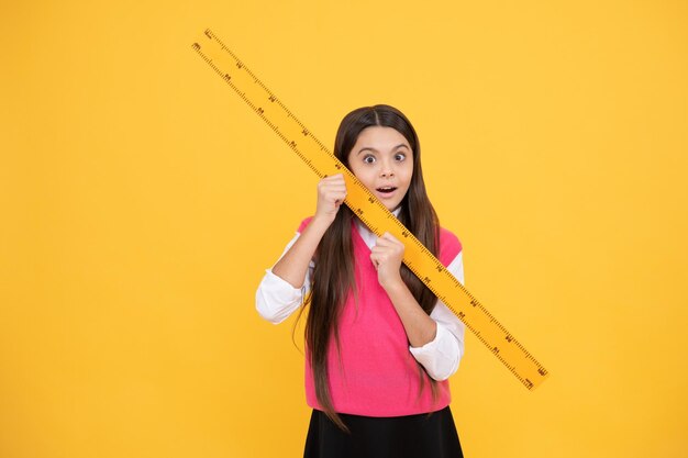 Una bambina stupita studia la geometria a lezione scolastica con le discipline dello stelo del righello