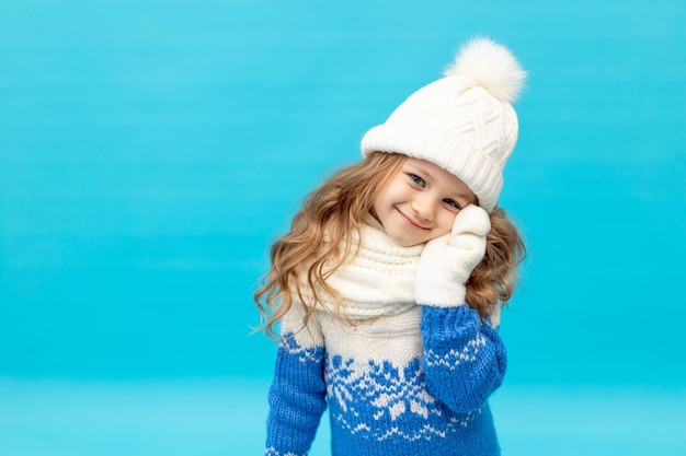 Una bambina su sfondo blu con un cappello invernale e un maglione con guanti sorride lo spazio per il testo