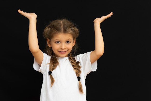 Una bambina su sfondo nero tiene il tuo annuncio con le mani.