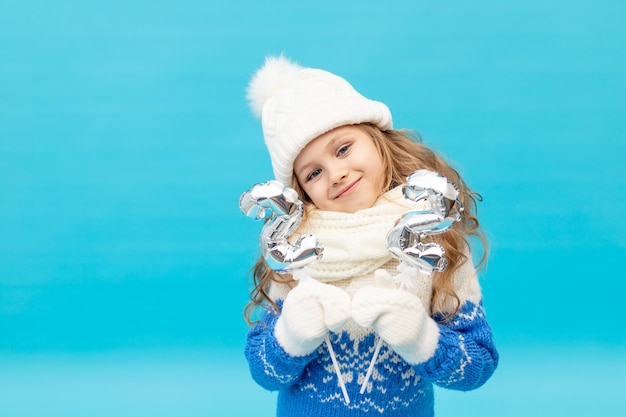 Una bambina su uno sfondo blu in studio con un cappello invernale e un maglione contiene i numeri 2 e 2, il concetto di capodanno e Natale, spazio per il testo