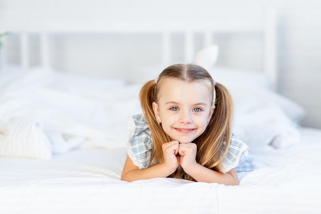 Una bambina sul letto di casa su un letto di cotone bianco giace e sorride dolcemente