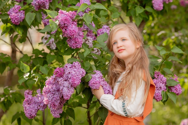 Una bambina tiene i fiori lilla in un giardino lilla in primavera