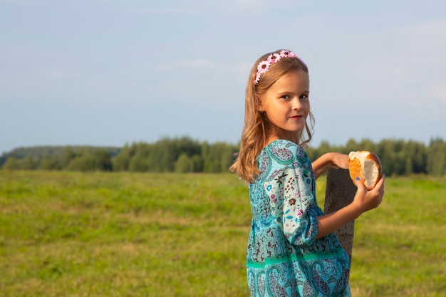 Una bambina tiene il pane in mano in un prato d'estate. Cuocere, pane in mano alla ragazza