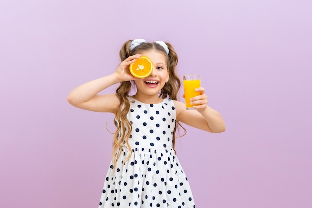 Una bambina tiene il succo d'arancia e un'arancia Un bambino in un vestito a pois beve succo appena spremuto