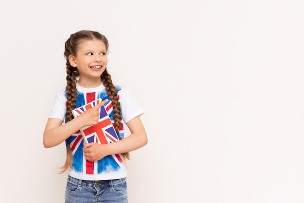 Una bambina tiene in mano un libro sull'inglese e sorride in modo sconvolgente su uno sfondo bianco e isolato