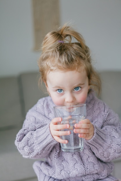 Una bambina tiene un bicchiere d'acqua, beve. Accogliente.
