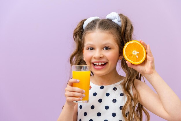 Una bambina tiene un bicchiere di succo d'arancia e una fetta di succo d'arancia appena spremuto per colazione vitamine naturali per i bambini