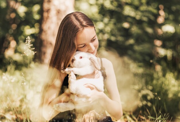 Una bambina tiene un coniglio bianco tra le braccia in natura in estate