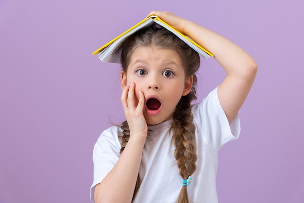 Una bambina tiene un libro come un tetto sopra la sua testa. Molto sorpreso.