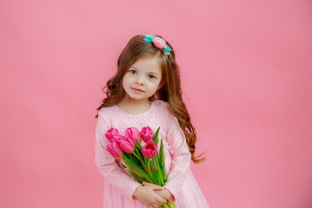 Una bambina tiene un mazzo di tulipani rosa su sfondo rosa