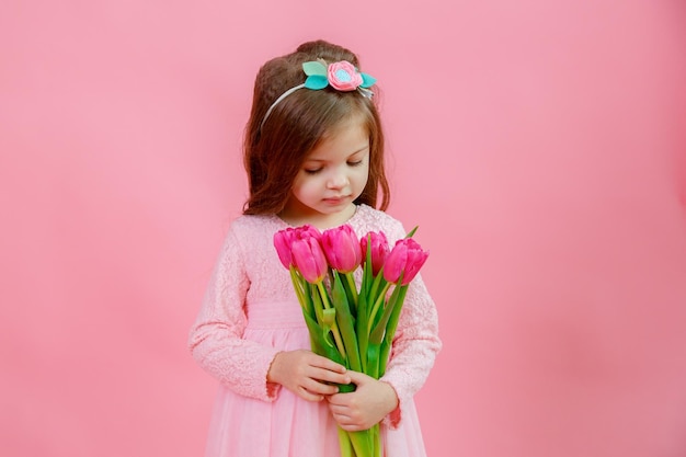 Una bambina tiene un mazzo di tulipani rosa su sfondo rosa