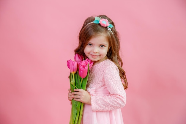 Una bambina tiene un mazzo di tulipani rosa su sfondo rosa