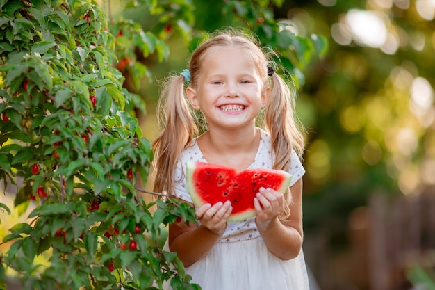 Una bambina tiene un pezzo di anguria al sole estivo