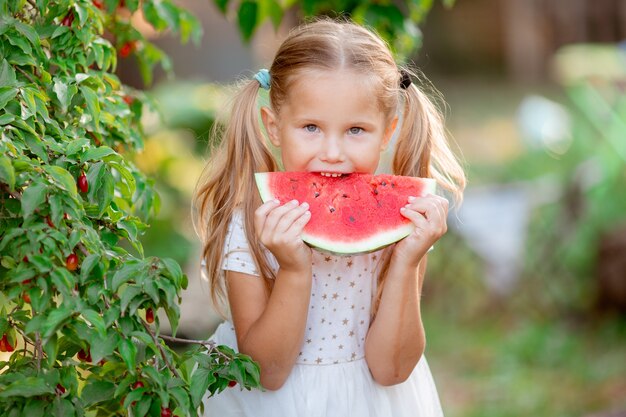 Una bambina tiene un pezzo di anguria al sole estivo