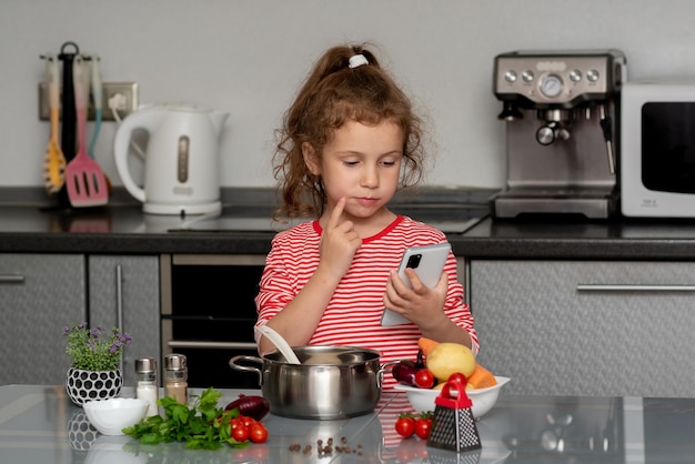 Una bambina tiene un telefono e pensa a cosa cucinare dalle verdure fresche Una corretta alimentazione Dieta