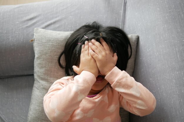 Una bambina triste si copre il viso con la mano sdraiata sul divano