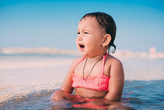 Una bambina, un bambino in costume da bagno rosa seduto in mare è molto felice e allegro