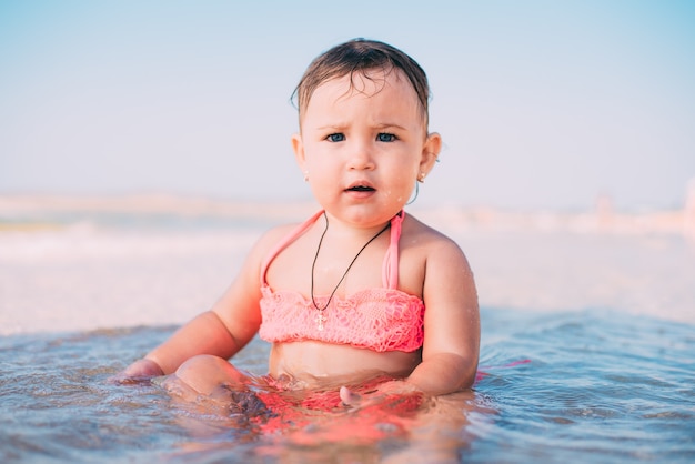 Una bambina, un bambino in costume da bagno rosa seduto in mare è molto felice e allegro