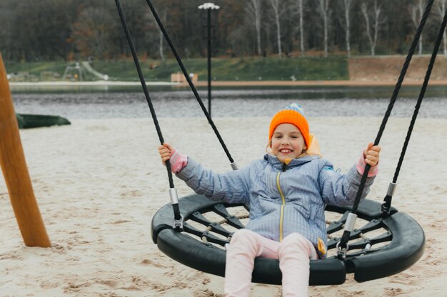 Una bambina va a fare un giro su un'altalena vicino a uno stagno in un parco autunnale. vacanza autunnale.