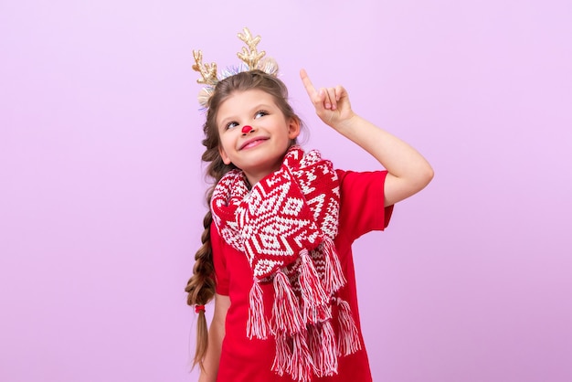 Una bambina vestita con orecchie di cervo sulla testa punta il dito verso l'alto e sorride.