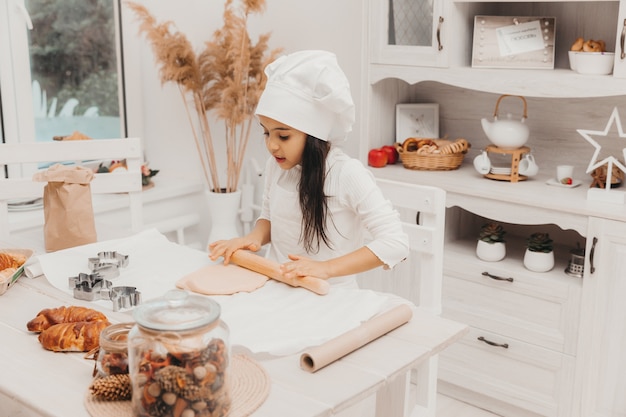 Una bambina vestita da cuoca in cucina prepara i biscotti.