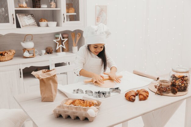 Una bambina vestita da cuoca in cucina prepara i biscotti.