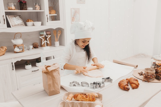 Una bambina vestita da cuoca in cucina prepara i biscotti.