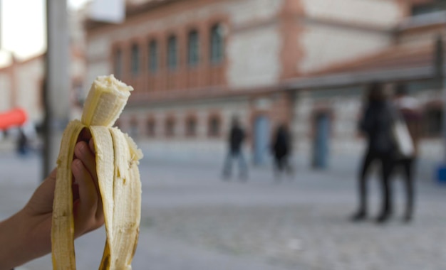 Una banana chiusa quasi finita per strada tenuta da una mano di bambino Concetto di cibo