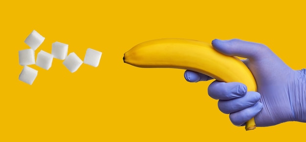 Una banana in una mano in un guanto medico blu spara lo zucchero. Alto contenuto di carboidrati veloci nella frutta dolce. Concetto di diabete