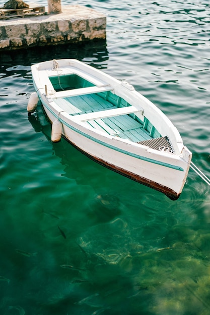 Una barca da pesca bianca con un fondo verde è ormeggiata a un molo di pietra
