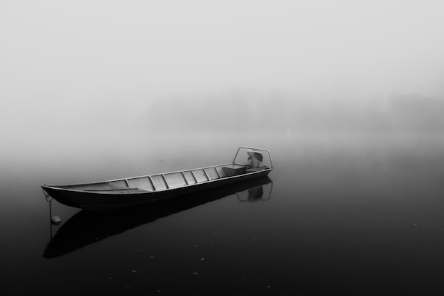 Una barca galleggia su un lago con la nebbia sullo sfondo.