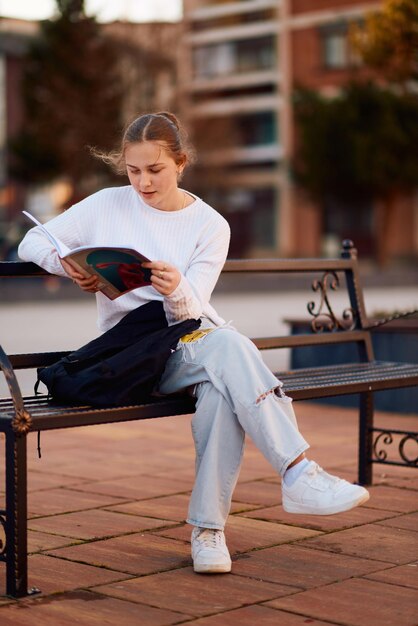 Una bella adolescente bionda si siede su una panchina nel parco facendo una pausa dalla scuola per immergersi