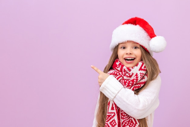 Una bella bambina è molto felice del Natale. Un bambino con il cappello di Capodanno punta il dito di lato.